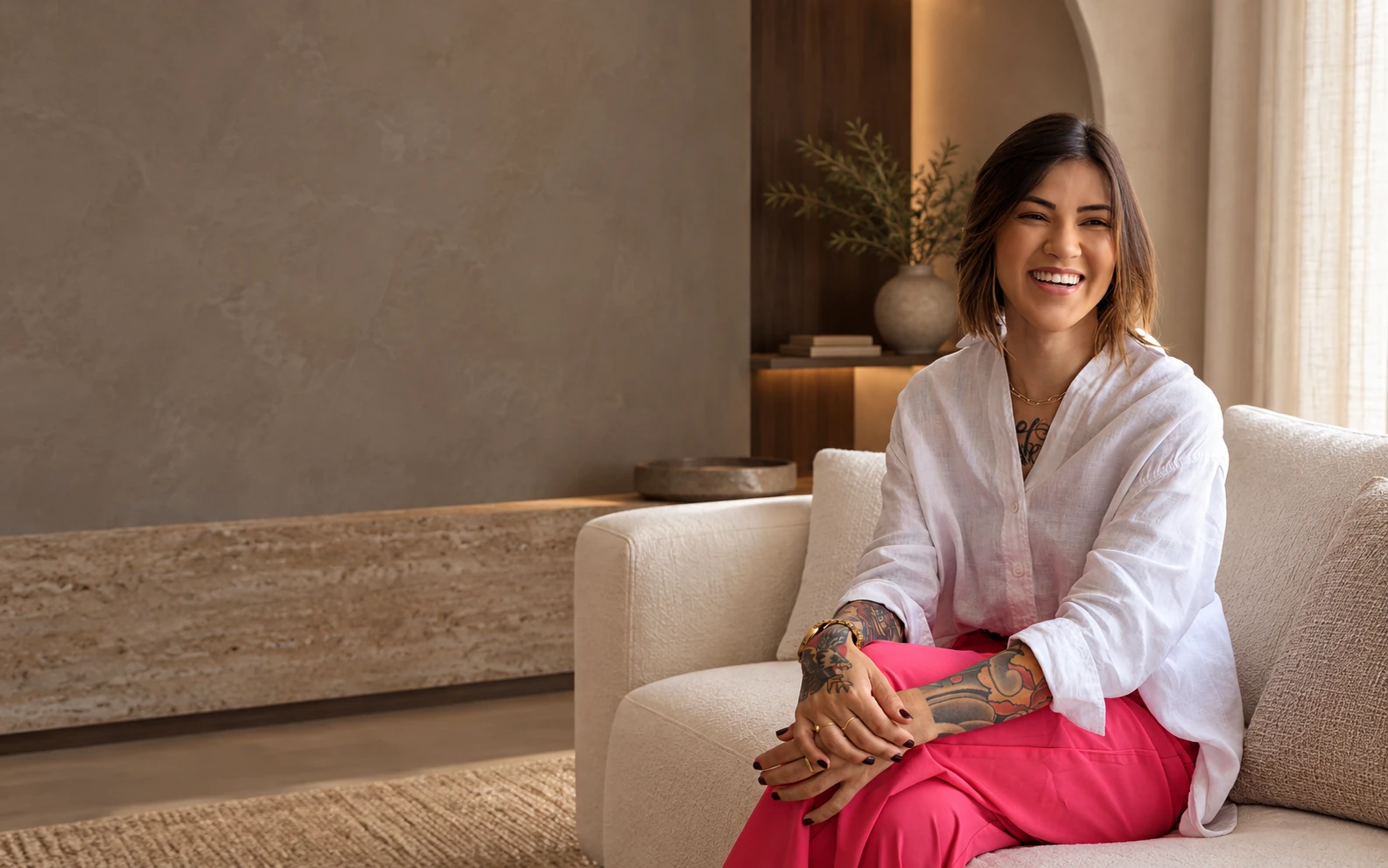 Dra. Thaís Ferrera sorrindo, sentada em um sofá em ambiente de tons quentes